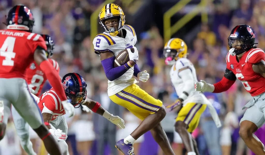 An LSU receiver leaps for a catch between Ole Miss defenders under the lights in a night game at Tiger Stadium