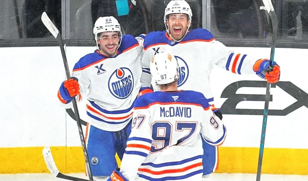 Connor McDavid and Edmonton Oilers teammates celebrate a goal in their white road jerseys.